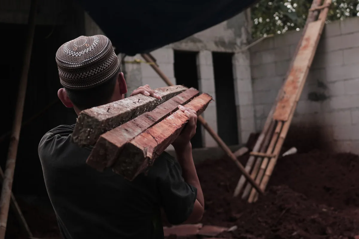 Ouvrier transportant des planches sur chantier, illustrant l'impact de l'accès et de la manutention sur le budget