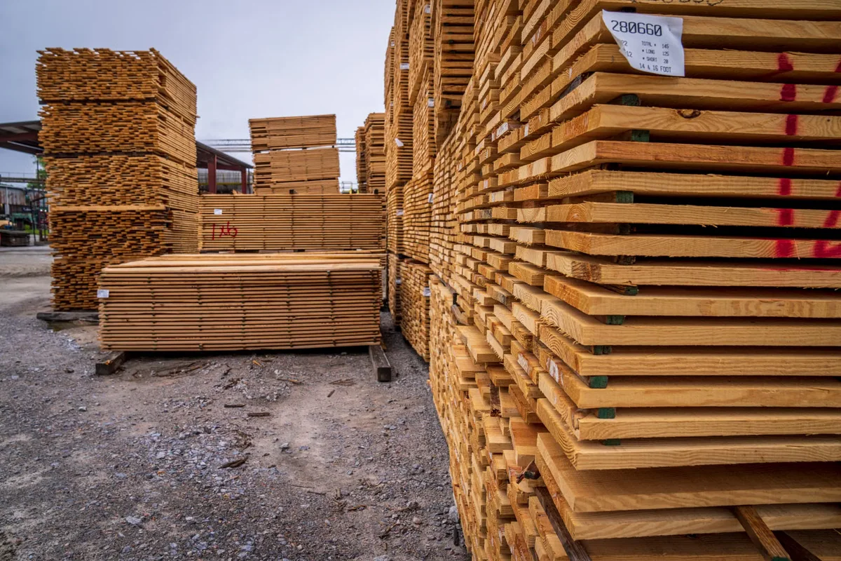 Lots de planches stockés en extérieur, illustrant le poste matière avant transport, coupe et pose