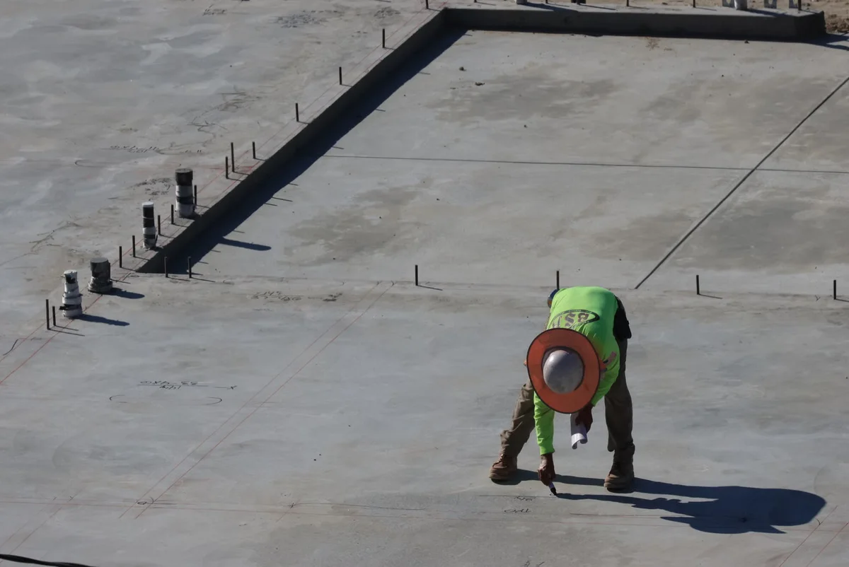Ouvrier sur une dalle en béton extérieure, illustrant l'impact du support sur un projet de petite terrasse