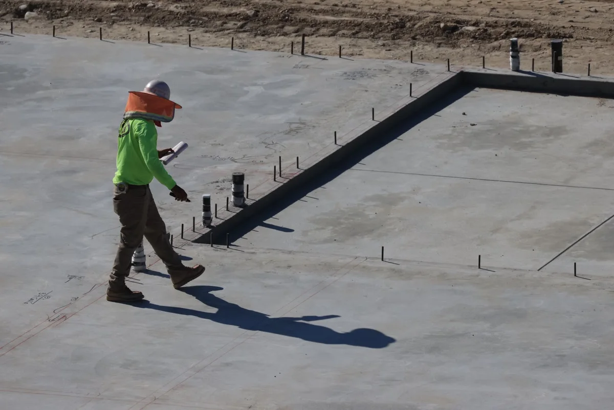 Professionnel inspectant une dalle en béton extérieure, illustration du diagnostic du support avant de choisir entre dalle et structure sur plots