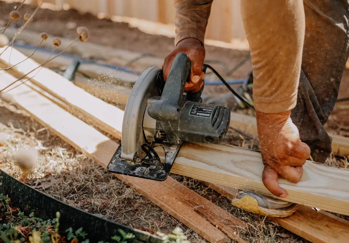 Artisan découpant des planches de bois en extérieur, illustration d'un remplacement ciblé de lames lors d'une rénovation