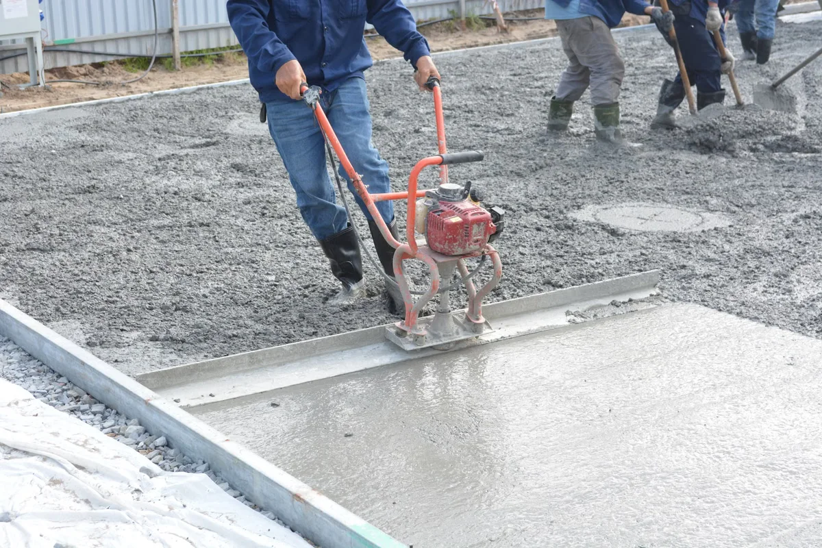 Équipe nivelant du béton frais sur chantier, illustrant coffrage, mise en œuvre et temps propre à une dalle