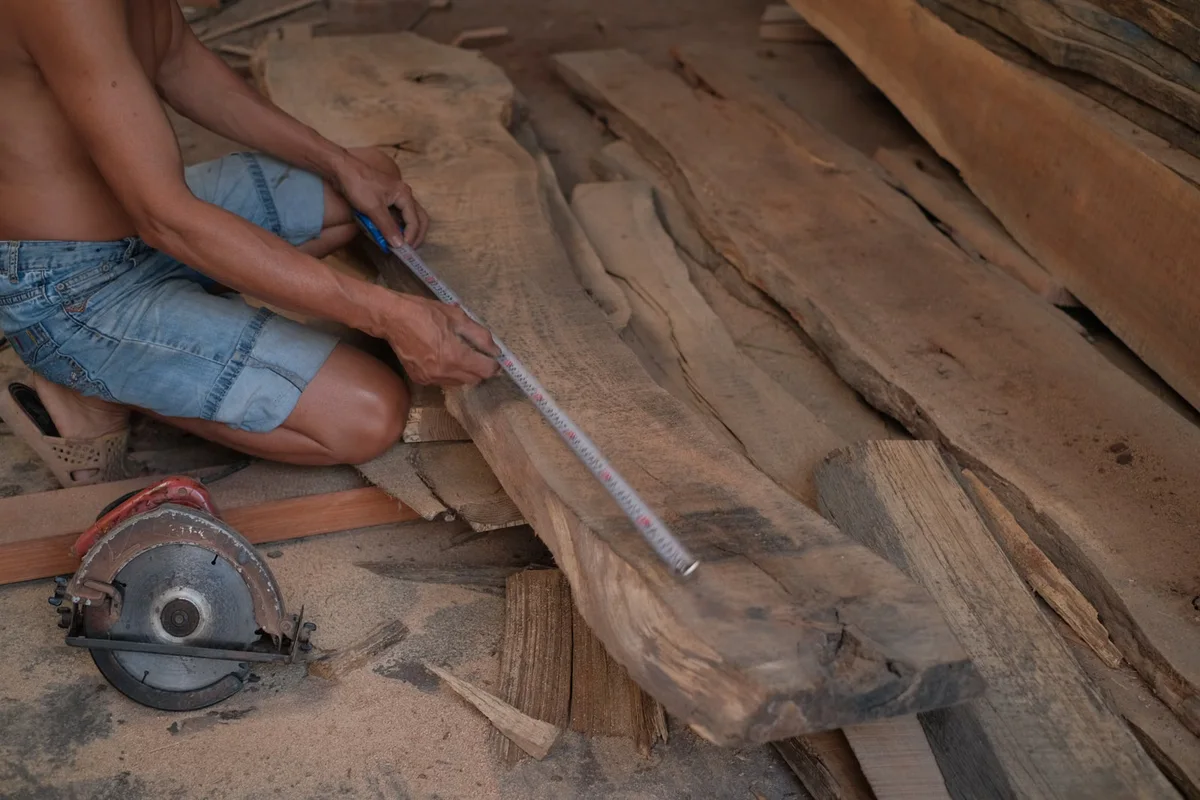Artisan mesurant précisément une pièce de bois, illustration du dimensionnement qui doit précéder l'ajout de charges particulières sur une terrasse