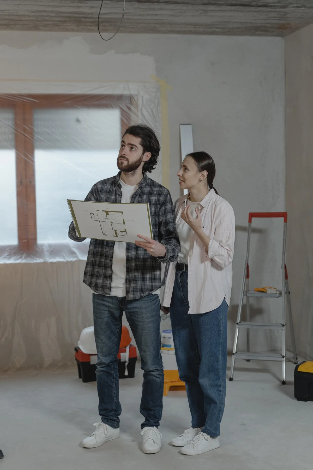 Couple consultant des plans dans un logement en rénovation, illustration d'un chantier d'amélioration sur un logement existant