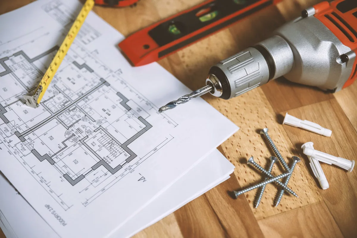 Plan de chantier, perceuse, vis et mètre ruban illustrant les différents postes d'un devis de terrasse