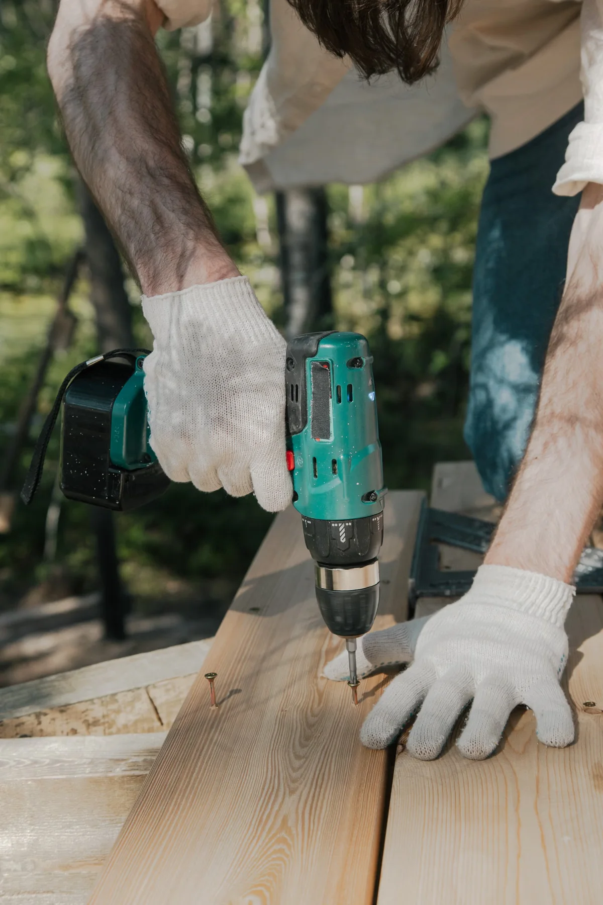 Vissage d'une planche en bois avec une perceuse en extérieur, illustration du positionnement et du choix des fixations d'une terrasse
