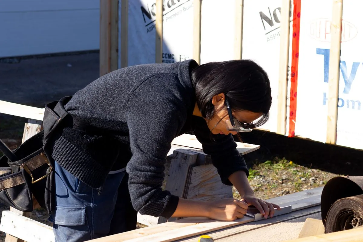 Charpentière mesurant et marquant une pièce de bois sur chantier, illustration d'un entraxe à déterminer par mesure et dimensionnement plutôt que par habitude