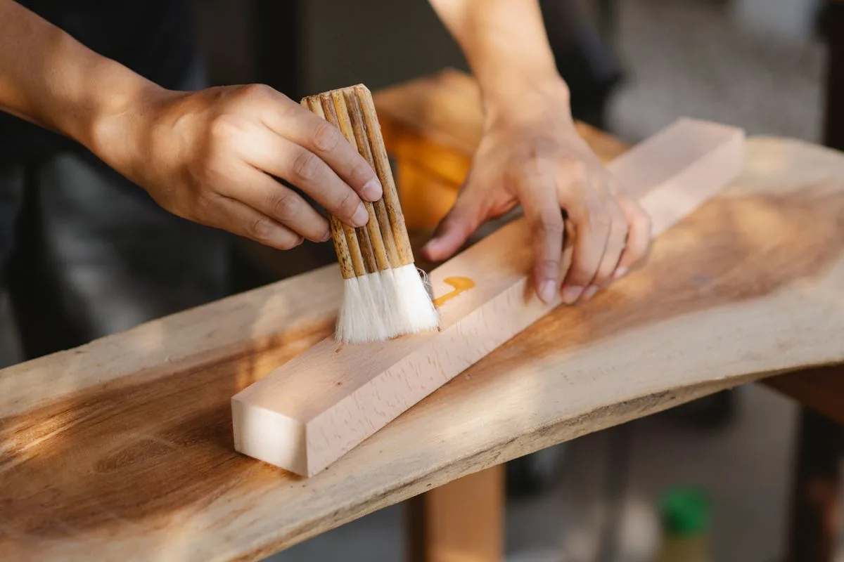 Artisan appliquant une huile au pinceau sur une planche de bois, illustration d'une finition destinée à préserver l'aspect d'une surface extérieure