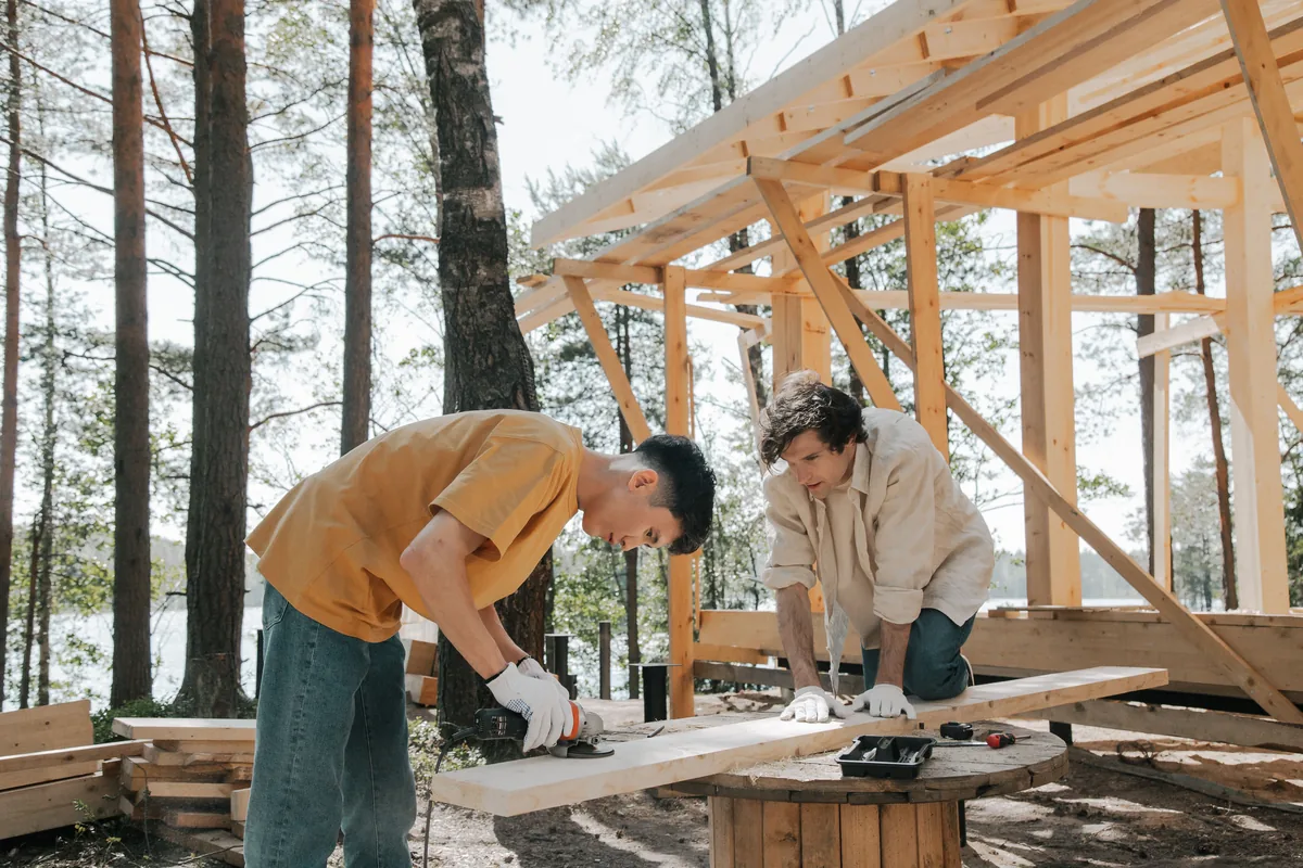 Deux charpentiers assemblant une structure en bois, illustration de la ventilation, des entraxes et de la précision nécessaires lors de la pose