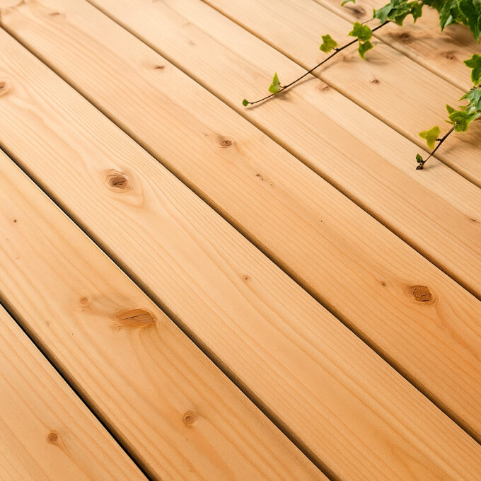 Lames de terrasse en bois Douglas rosé, avec veinage naturel et nœuds visibles, posées en extérieur sous une lumière naturelle.